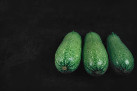 Three zucchini on a dark background. Organic eco food. Healthy diet. Freshly picked vegetables. Fresh greens for salad. Natural organic food. Edible vegetable backgroundの写真素材