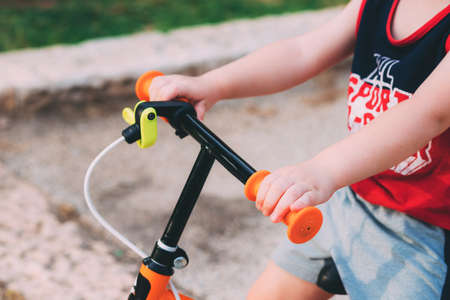 Blurred child sits on a bicycle. Father's day. Child's hands on the hand of an orange bike for...
