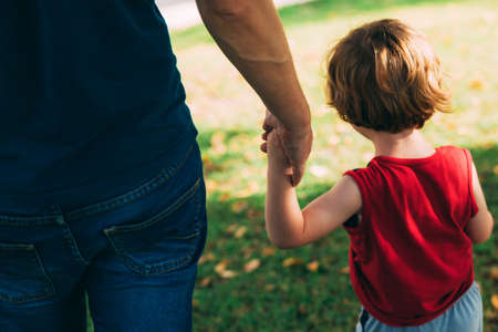 Father's day. Dad and son. Dad holds the hand of a little son in the park. Little child holding hands with his father outdoors. Family time. Close-up. Adult and child hands on natural backgroundの写真素材