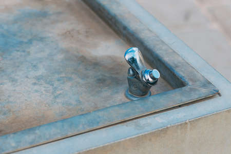 Water drinking fountain in public area. Close-up view of dry closed drinking fountain. Aluminum dirty sink and chrome faucet with button to open water in public park. Free drinking water fountainの写真素材