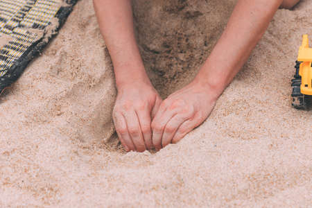 Father's day. Man's hands digging a hole in the sand to build a deep tunnel. Games in the sand with a child. Toy cars. Entertainment for children and adults. It's more fun together. Two handsの写真素材