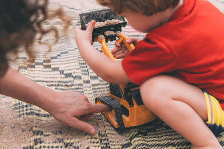 Father's day. Dad and son. Little son plays toys with dad on the beach with sand. Happy loving family. Happy family father and child. Toy cars. Hands of a man and a small child on the beach. Togetherの写真素材