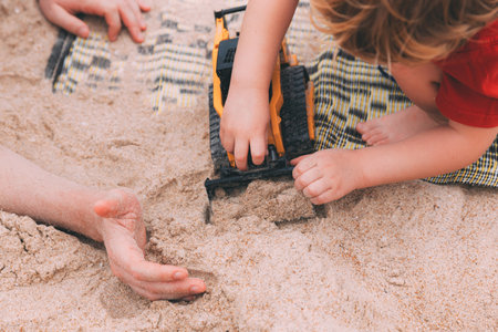 Father's day. Dad and son. Little son plays toys with dad on the beach with sand. Happy loving family. Happy family father and child. Toy cars. Hands of a man and a small child on the beach. Togetherの写真素材