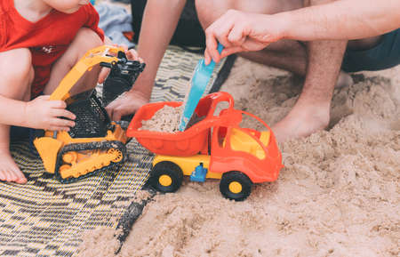 Fathers day. Dad and son. Little son plays toys with dad on the beach with sand. Happy loving family. Happy family father and child. Toy cars. Hands of a man and a small child on the beach. Togetherの写真素材