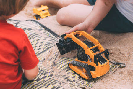 Father's day. Dad and son. Little son plays toys with dad on the beach with sand. Happy loving family. Happy family father and child. Toy cars. Hands of a man and a small child on the beach. Togetherの写真素材