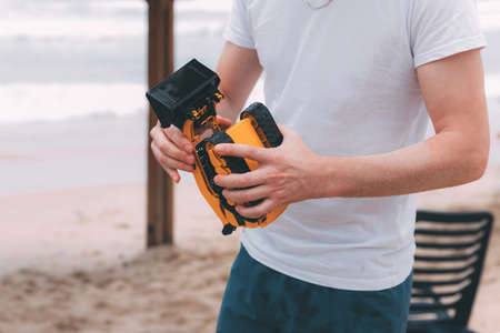 Father's day. Young dad in a white T-shirt and seated shorts holds in his hands an orange toy car on the beach. Happy loving family. A happy family. Dad is repairing a toy for his child.の写真素材