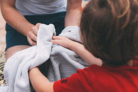 Father's day. Dad and son. Dad wipes his son's hands with a towel on the beach. Happy family father and child. Hands of a young man and his son blurred in the foreground from back. After washing handsの写真素材