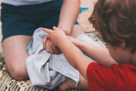 Father's day. Dad and son. Dad washes his son his hands with water from a bottle on the beach. Happy family father and child. Hands of a young man and his son blurred in the foreground from backの写真素材