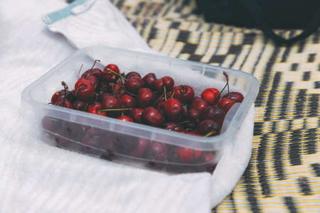 Ripe sweet cherries in a boxing box on a bedspread on the beach. Cherry season in early summer. Ripe berries. Organic food. What to eat on the beach. Healthy and tasty foodの写真素材