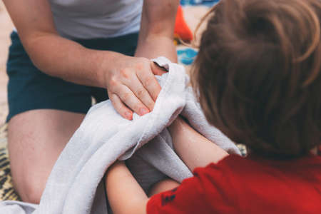 Father's day. Dad and son. Dad wipes his son's hands with a towel on the beach. Happy family father and child. Hands of a young man and his son blurred in the foreground from back. After washing handsの写真素材
