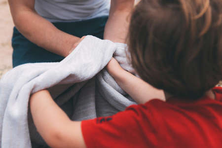 Father's day. Dad and son. Dad wipes his son's hands with a towel on the beach. Happy family father and child. Hands of a young man and his son blurred in the foreground from back. After washing handsの写真素材