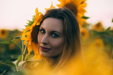 Girl in a green dress and long blond hair in a sunflower field, smiles and enjoys the moment. The concept of summer and sun. Sunflower season in Israel. Celebrating life.の写真素材
