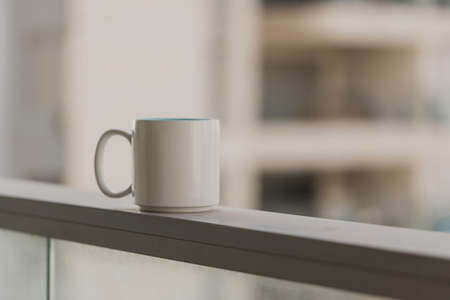 Close-up view of white blue coffee cup on sky terrace border on balcony with blurred morning city scape background. Selective focus and copy space. Beverage, breakfast. Hot tea in the mug. Morningの写真素材
