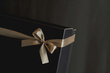 Close-up view of black gift box with elegant golden ribbon in luxury bow on dark background. Gift...