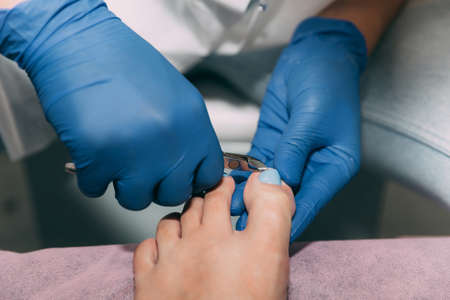 Pedicure process in salon. Foot care treatment and nail. Removing dead skin with forceps. Master in blue gloves makes pedicure with manicure machine. Concept of beauty care and health.の写真素材