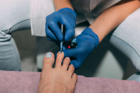 Pedicure process in salon. Foot care treatment and nail. Applying gel polish to nails with a brush. Master in blue gloves makes pedicure with manicure machine. Concept of beauty care and health.の写真素材