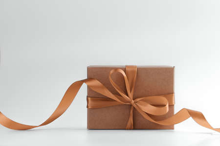 Brown gift box with gold bow and ribbon on white background. Holiday greeting card. Wrapped vintage...