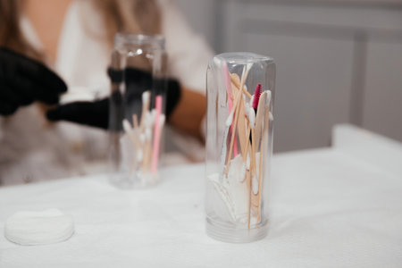 Tools for permanent makeup inside the bottle in focus and blurred hands of female master in black gloves on background. Sterility of tattoo instruments. Beautician tools for making eyebrows makeup.の写真素材