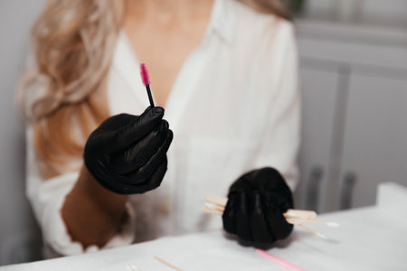 Pink brush for permanent makeup in hands of female master in black gloves, selective focus....