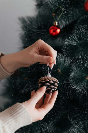 Women's beautiful hand wearing a brown sweater decorate the Christmas tree with toys and balls....