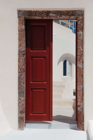 Half opened beautiful red door on white facade of greek architecture in Oia city, Santorini island, Greece, Europe. Beautiful details of the island of Santorini. famous travel destinationの写真素材