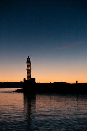 View of old venetian harbor waterfront and lighthouse at sunset time in old harbor of Chania, Crete, Greece. People silhouettes watching sunset at Chania Lighthouse on Crete, Greece. copy spaceの写真素材