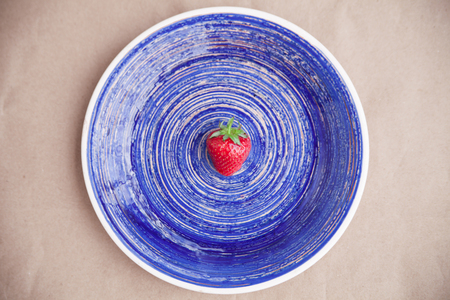 One berry of ripe strawberry on a bright blue dish. Healthy eating concept. Flat layの写真素材