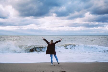 Winter sea. Storm waves and clouds. Young girl welcomes the elementsの写真素材