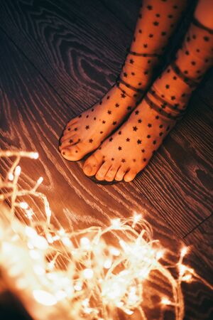 Female legs in socks with stars and christmas lights. On the eve of the holidayの写真素材