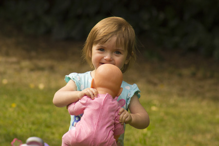 beautiful little girl playing with her baby doll in the gardenの写真素材