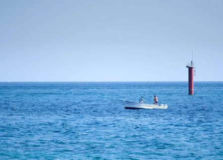 Two fishermen in a small boat fishing near lighthouseの写真素材
