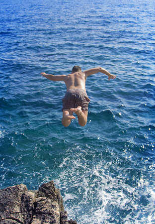 Boy jumping from a rock  into blue waterの写真素材
