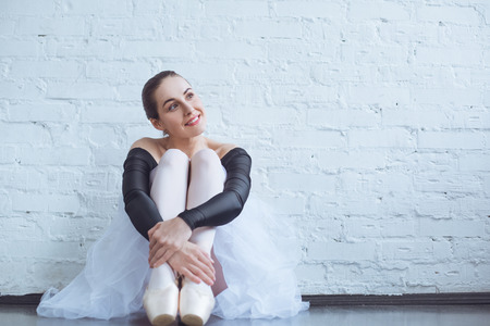 Young ballet dancer sitting leaning white wall in studio dreaming active lifestyleの写真素材