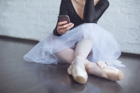 Young ballet dancer sitting leaning white wall using phone in studio active lifestyle close-upの写真素材