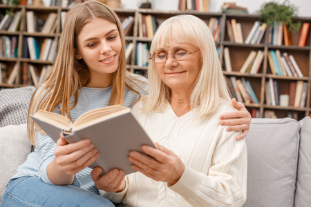 Granddaughter taking care of her retired grandmother reading bookの写真素材