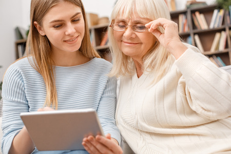 Granddaughter taking care of her retired grandmother using digital tabletの写真素材