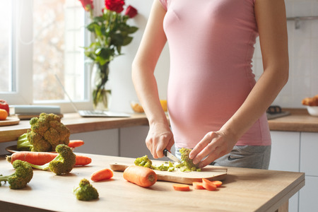 Young pregnant woman in the kitchen at home maternity concept cooking salad close-upの写真素材