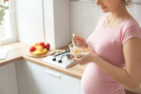 Young pregnant woman in the kitchen at home eating breakfast close-upの写真素材