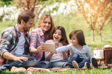 Family together outdoors in the park weekend concept picnic browsing internet surprisedの写真素材