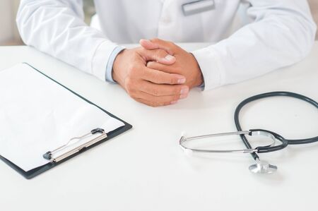 Senior man doctor at his office in clinic close-up sitting still palms together in a lock top viewの写真素材