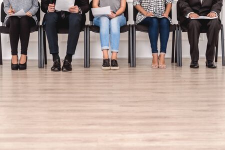 Group of people candidates men and women sitting on chairs waiting for job interview holding resume...