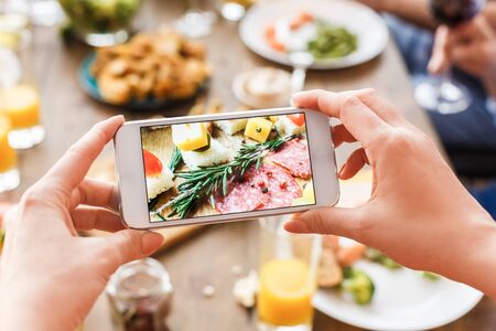 Cropped view of adult woman making photo with food on her modern smartphone, while she celebrate traditional hanukkah dinner together with familyの写真素材