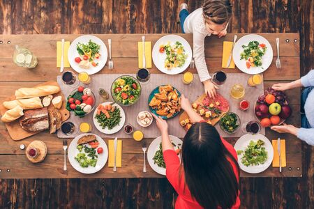 Young woman and her daughter, grandma putting food on table. Festive table set for six people. Wooden background top view mock-upの写真素材