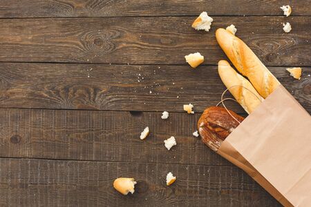 Flat lay view of pack of crafting paper bag with different, tasty and fresh french baguette, bread on wooden table with copy spaceの写真素材
