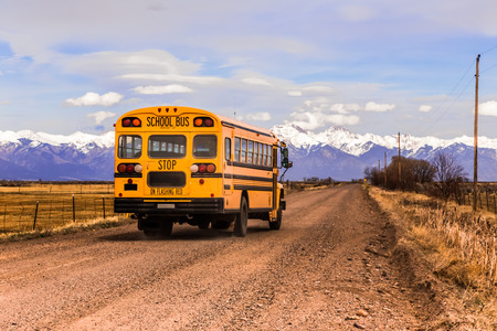 Yellow school bus on a country road, with snow-covered mountains in the background.の写真素材
