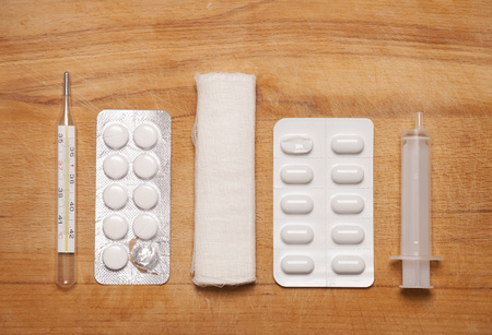 Home first aid kit: a thermometer, pills, bandages, syringe on wooden background.の写真素材