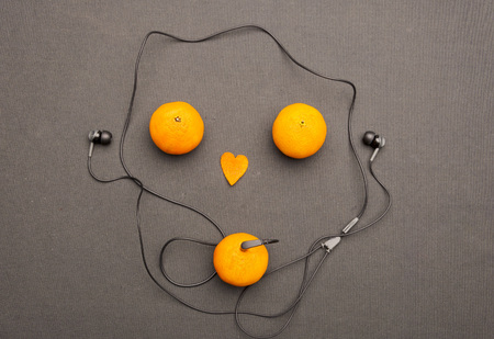 Funny fruity music player: headphones coming from of mandarin on a black background. Small orange heart and two mandarins lying near him in the form of face. Present for music and fruit lovers.の写真素材