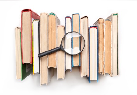 Stack of hardback books with magnifying glass isilated on white background, top view. Search for relevant and necessary information in a large number of sources during studies or work.の写真素材