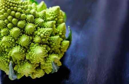 Close up view of amazing Romanesco broccoli or Roman cauliflower on wet dark blue background. Its form is a natural approximation of a fractal.の写真素材