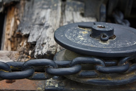 Black metal pulley with thick chain on woodの写真素材